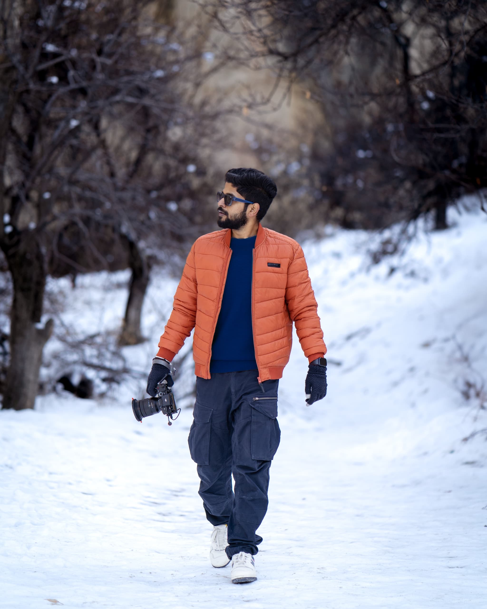 Photographer Shantanu Khare on a snow-lined Himalayan trail, camera in hand, in an orange jacket.