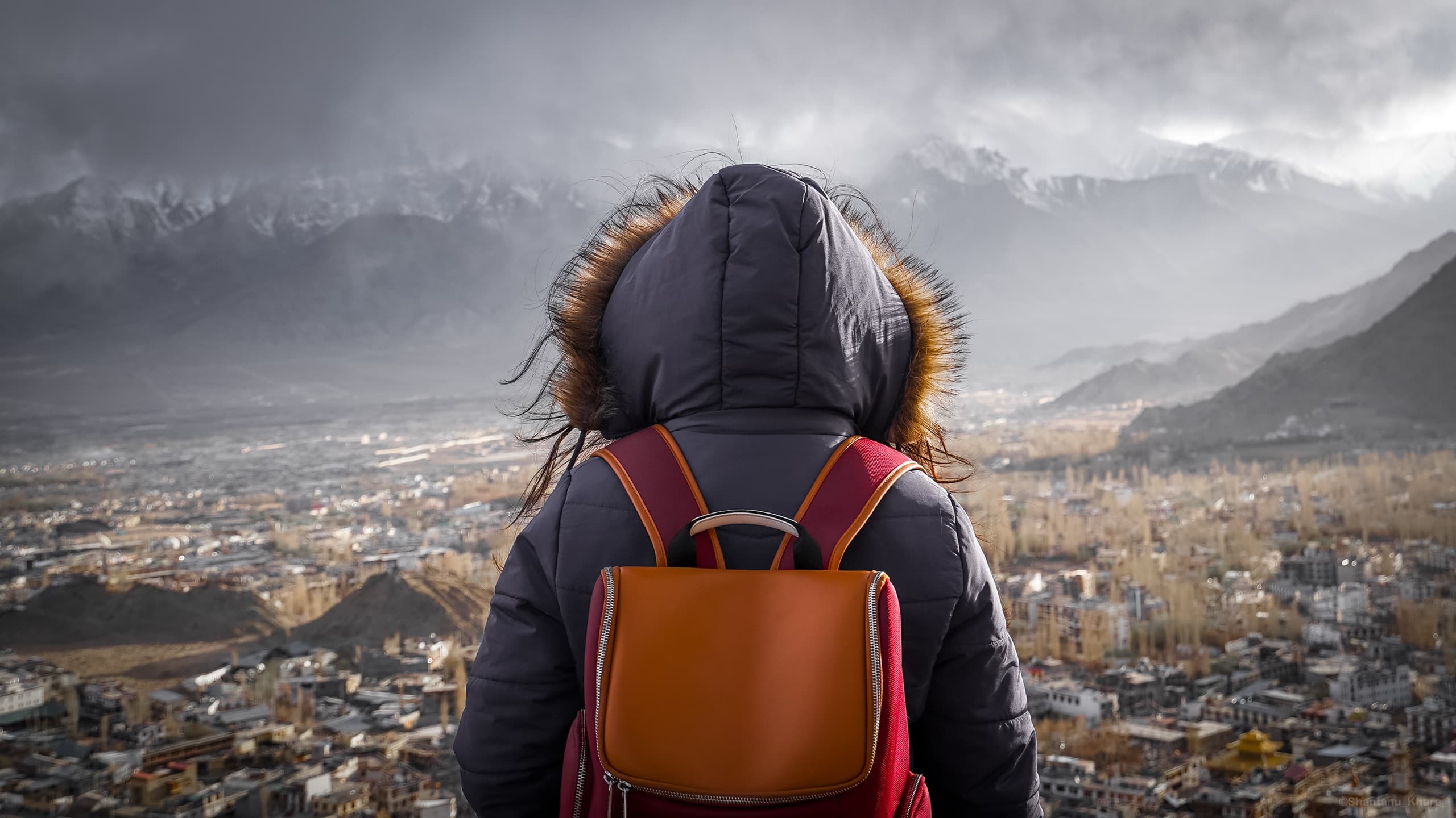 Travel portrait photography — a lone traveller looks out over the Leh valley and snow-capped Himalayan peaks, Ladakh.