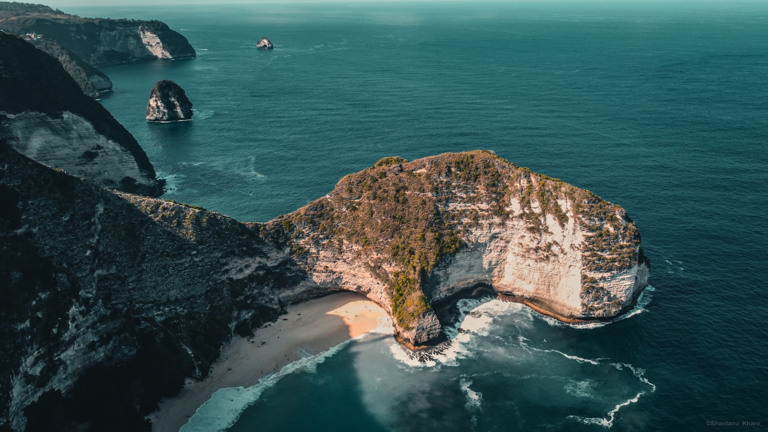 Aerial drone photography of Kelingking Beach — a cliff peninsula and hidden white-sand cove, Nusa Penida, Bali.