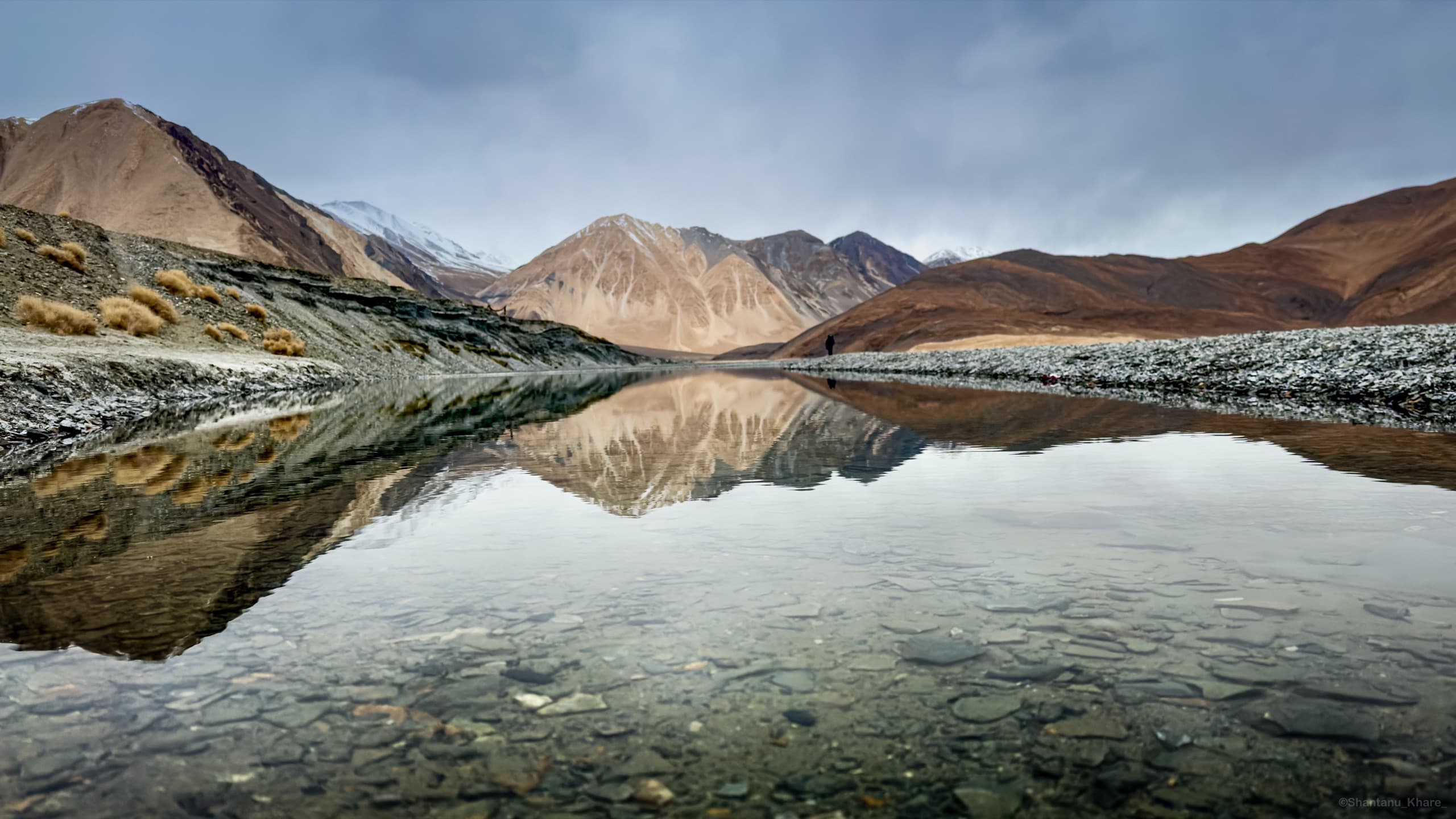 Landscape photography — barren mountains mirrored in Pangong Lake, Ladakh, a lone figure on the far shore.