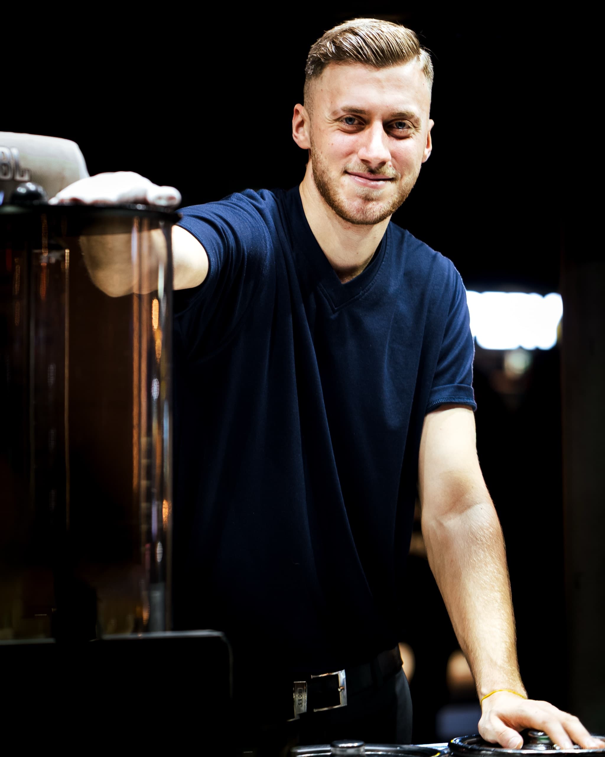 Environmental portrait photography — a barista at the counter of a dim café.