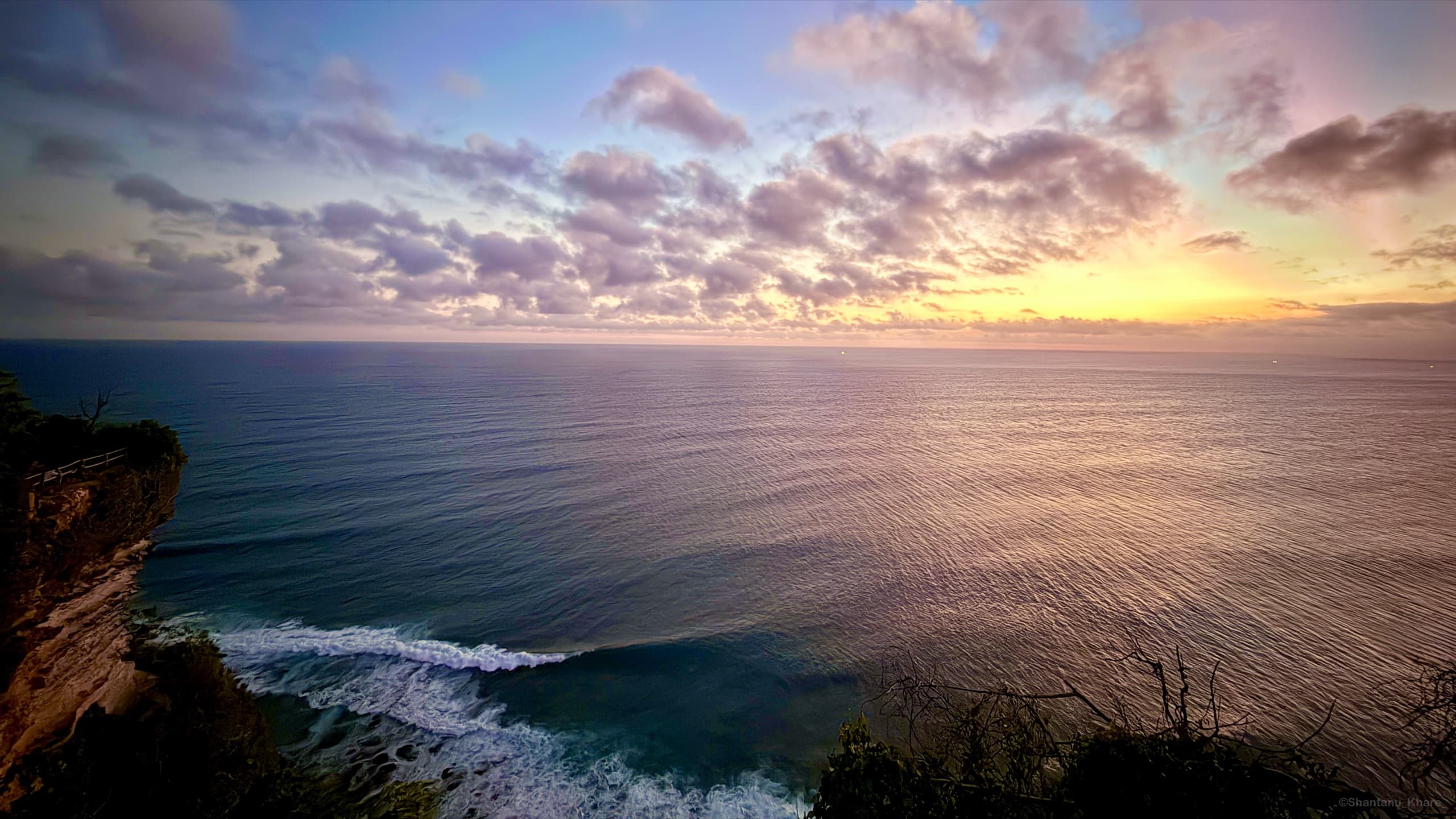 Landscape photography — waves rolling toward sea cliffs under a pastel sunset sky.