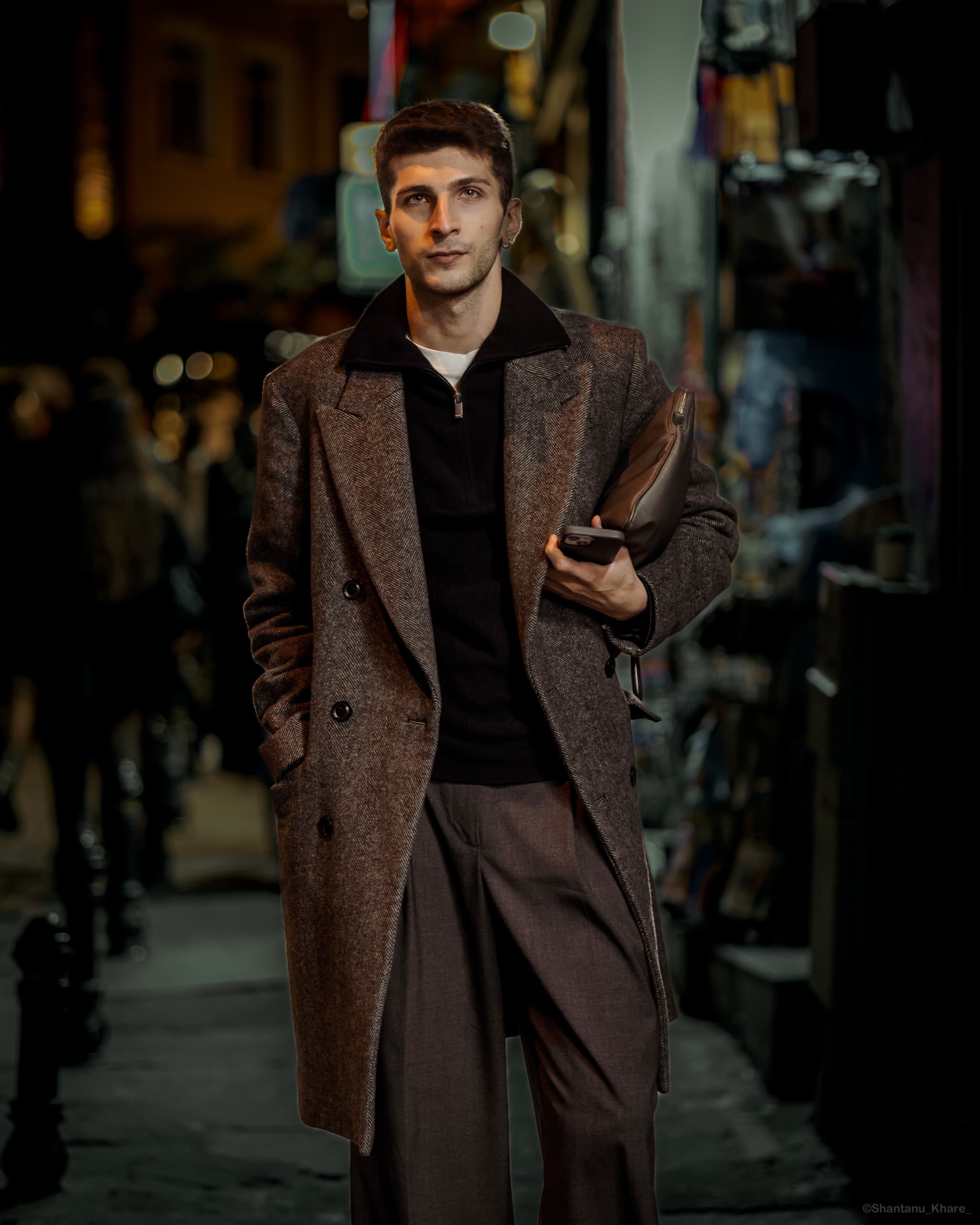 Night street portrait photography — a man in a herringbone overcoat with a leather clutch on a lamplit street.