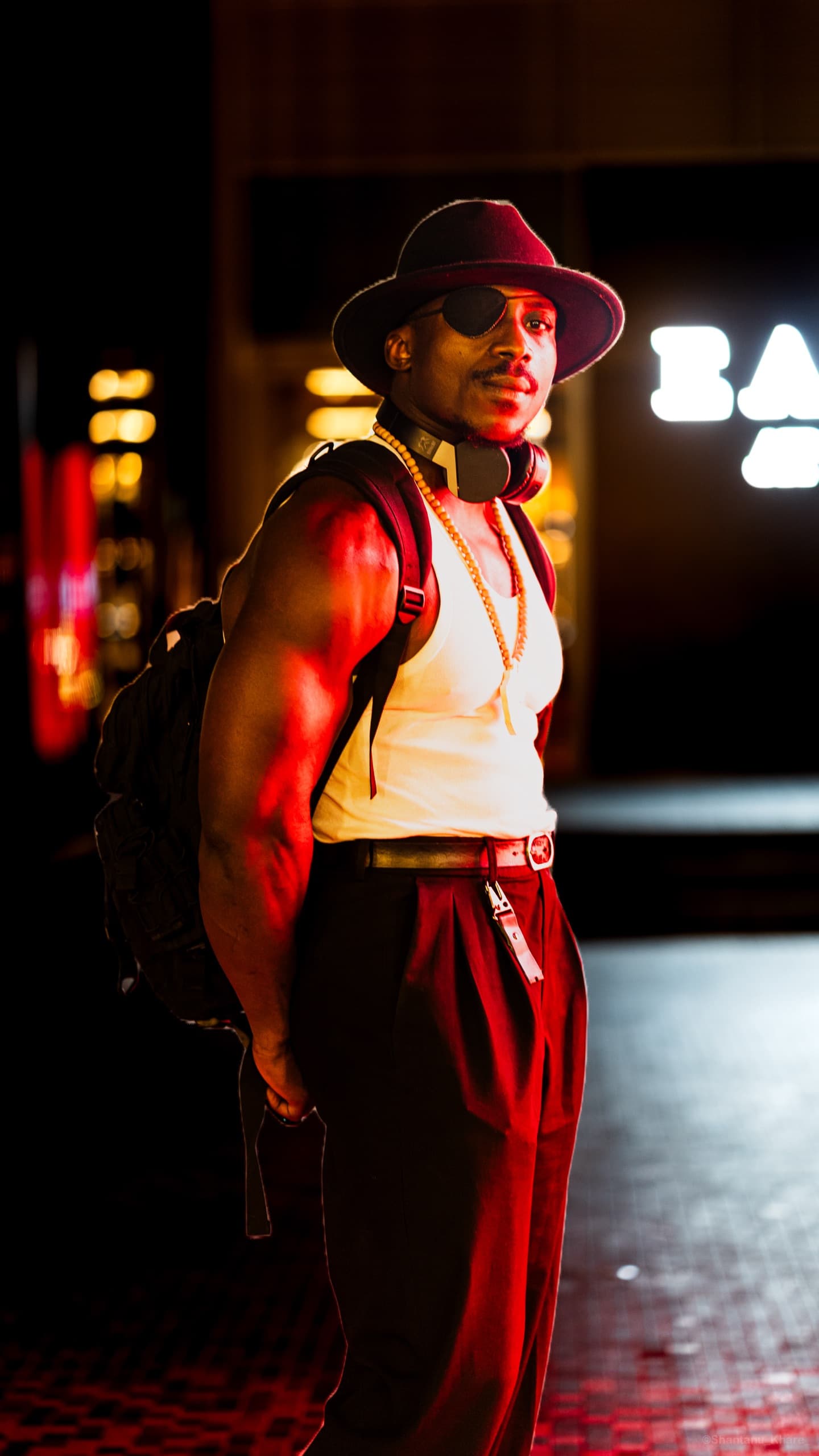Portrait photography — a man in a felt hat and headphones in warm neon light on a city street at night.